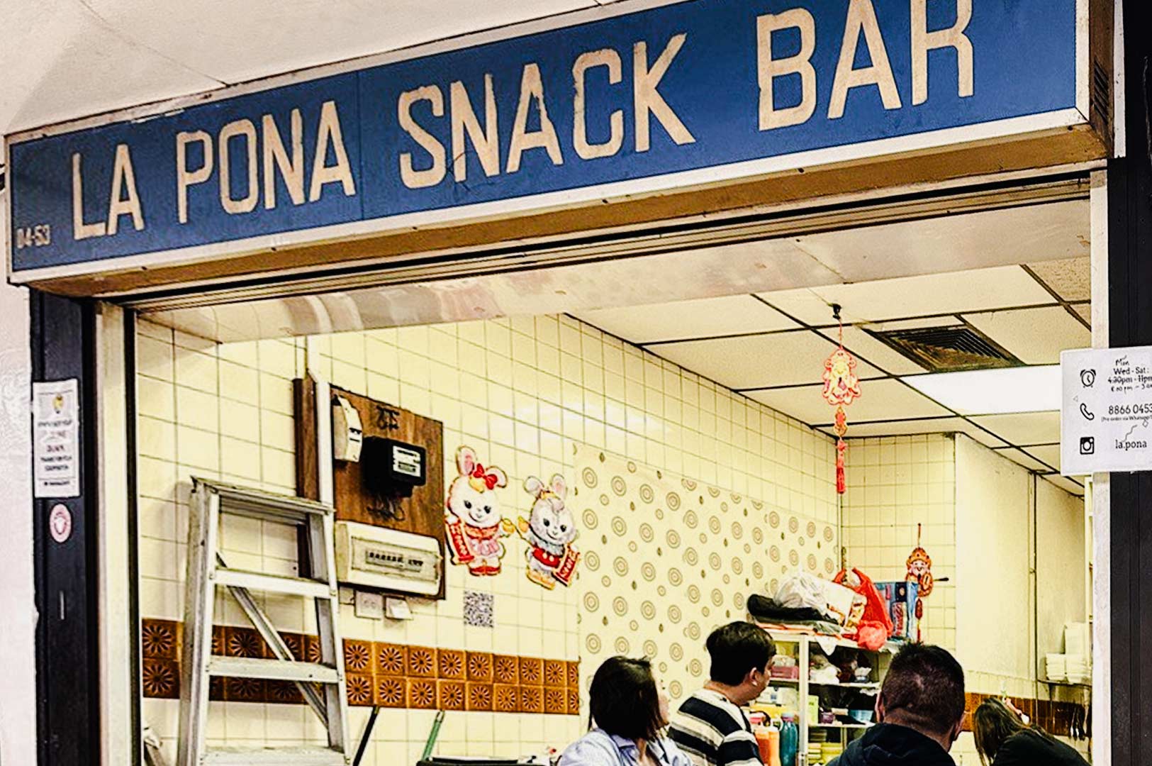 Exterior of La Pona Snack Bar with a vintage blue signboard, tiled interior, traditional décor, and customers ordering food at the counter.
