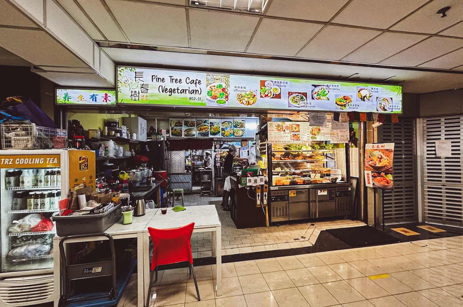 ine Tree Cafe vegetarian food stall, brightly lit signboard with English and Chinese text, menu featuring vegetarian bee hoon, curry, laksa, fish soup, tom yam, and spring rolls.