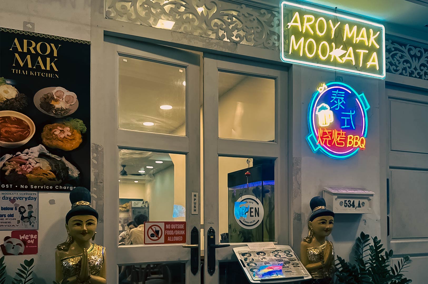 Exterior of Aroy Mak Mookata restaurant with neon signage and menu display at the entrance.