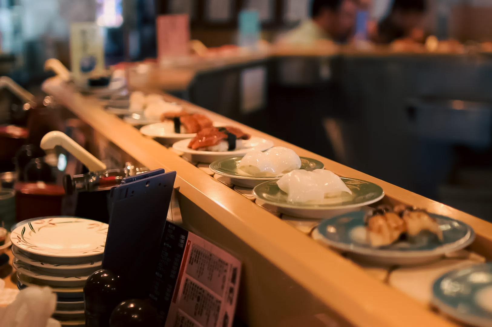 Assorted sushi plates on a conveyor belt at Genki Sushi, including nigiri and other Japanese dishes.