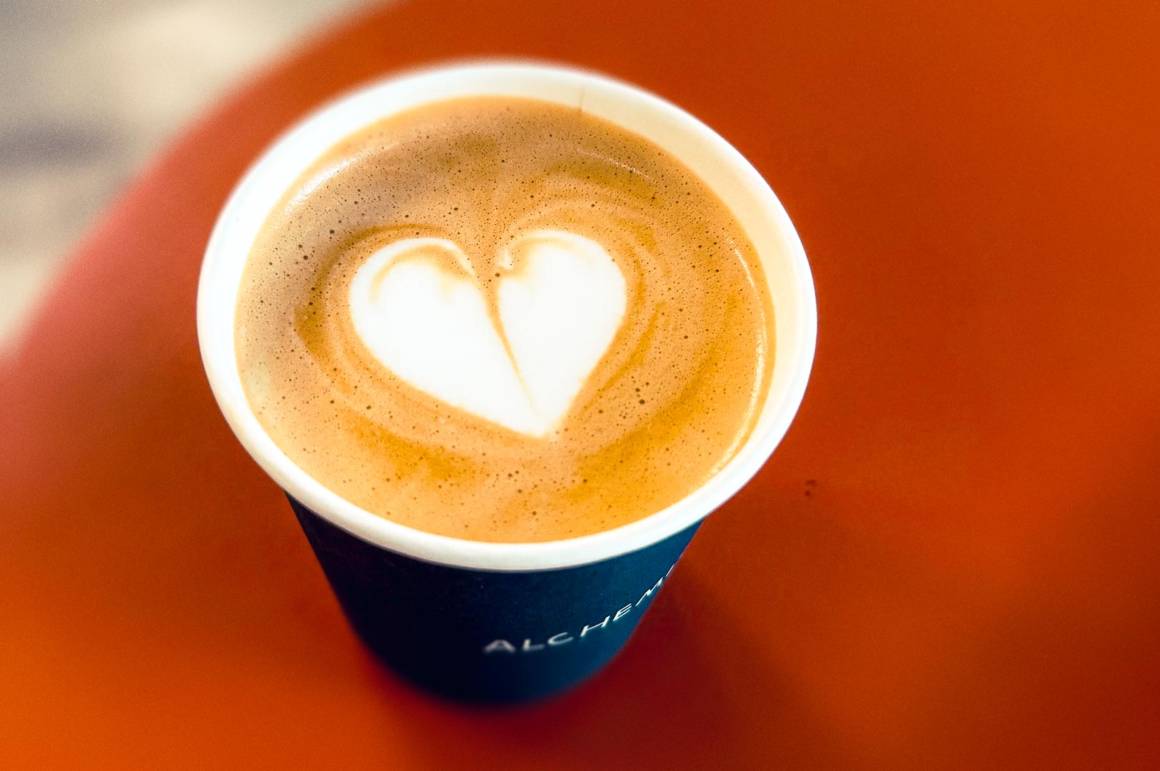 Cup of coffee with heart-shaped latte art on a warm orange tabletop.