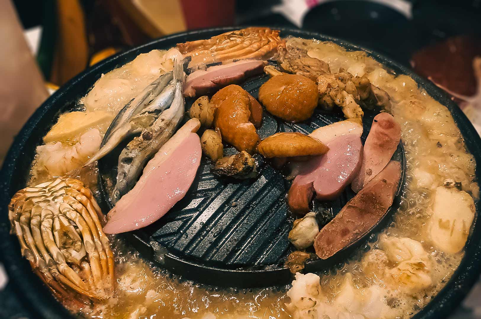 Mookata hotpot grill filled with assorted meats, seafood, mushrooms, and vegetables simmering in broth.