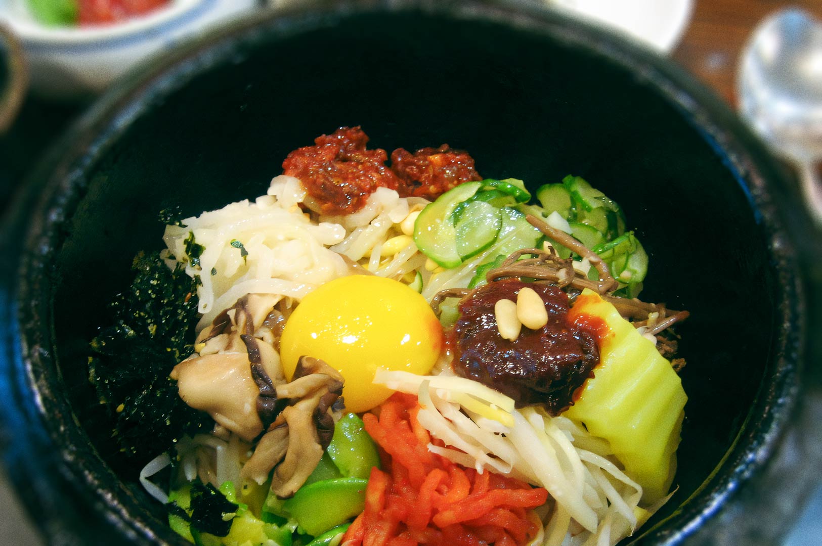 Bibimbap bowl with vegetables, raw egg yolk, and gochujang in a stone pot.