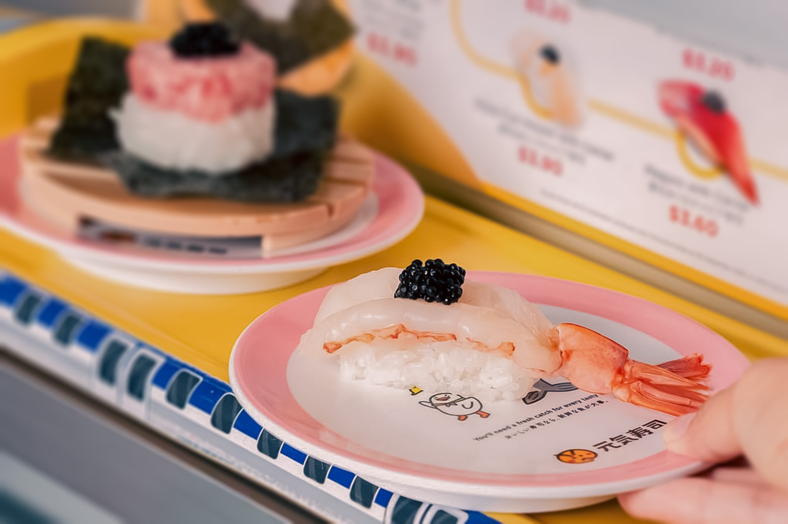 Close-up of shrimp and white fish sushi topped with caviar on a pink-rimmed plate at Genki Sushi.