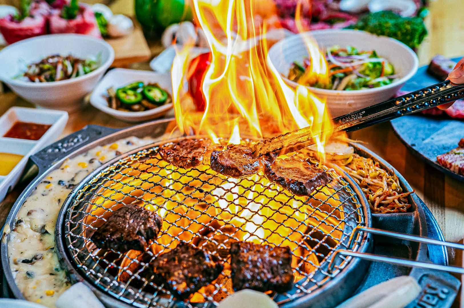 Korean BBQ meat grilling over open flame on a tabletop grill.