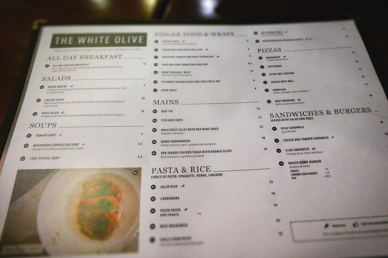 Menu from The White Olive featuring sections for all‑day breakfast, salads, soups, mains, pasta and rice, finger food, pizzas, and sandwiches, displayed in a clean black‑and‑white layout.