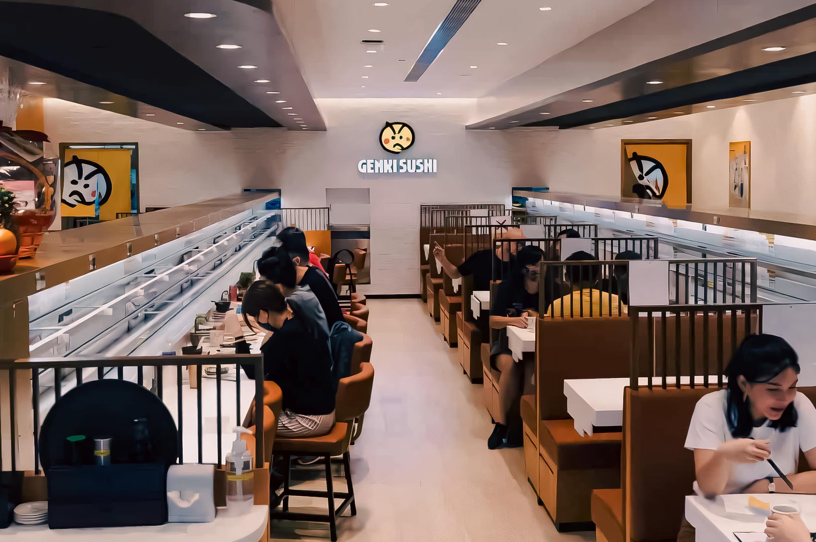 Interior of Genki Sushi Singapore with customers seated in booth-style tables beside automated conveyor belts.