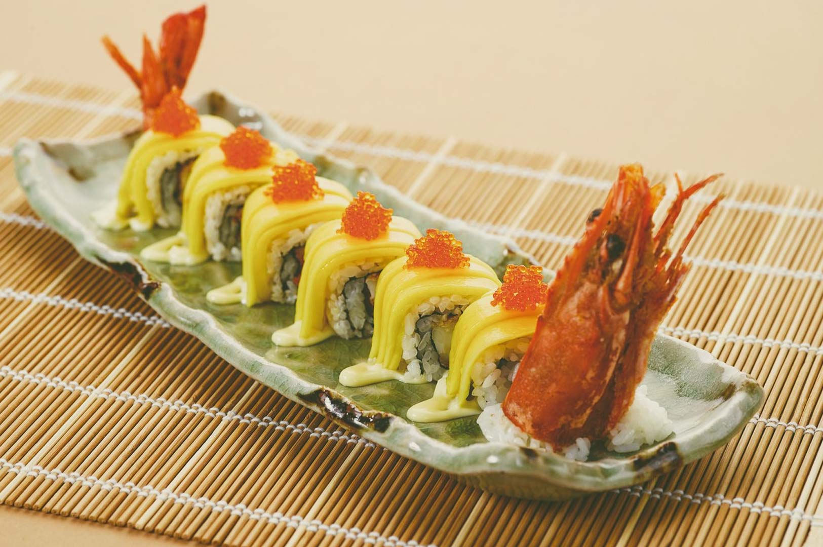 Sushi Tei Golden Roll sushi dish with mango slices, fish roe, creamy drizzle, and decorative shrimp presentation on bamboo mat.