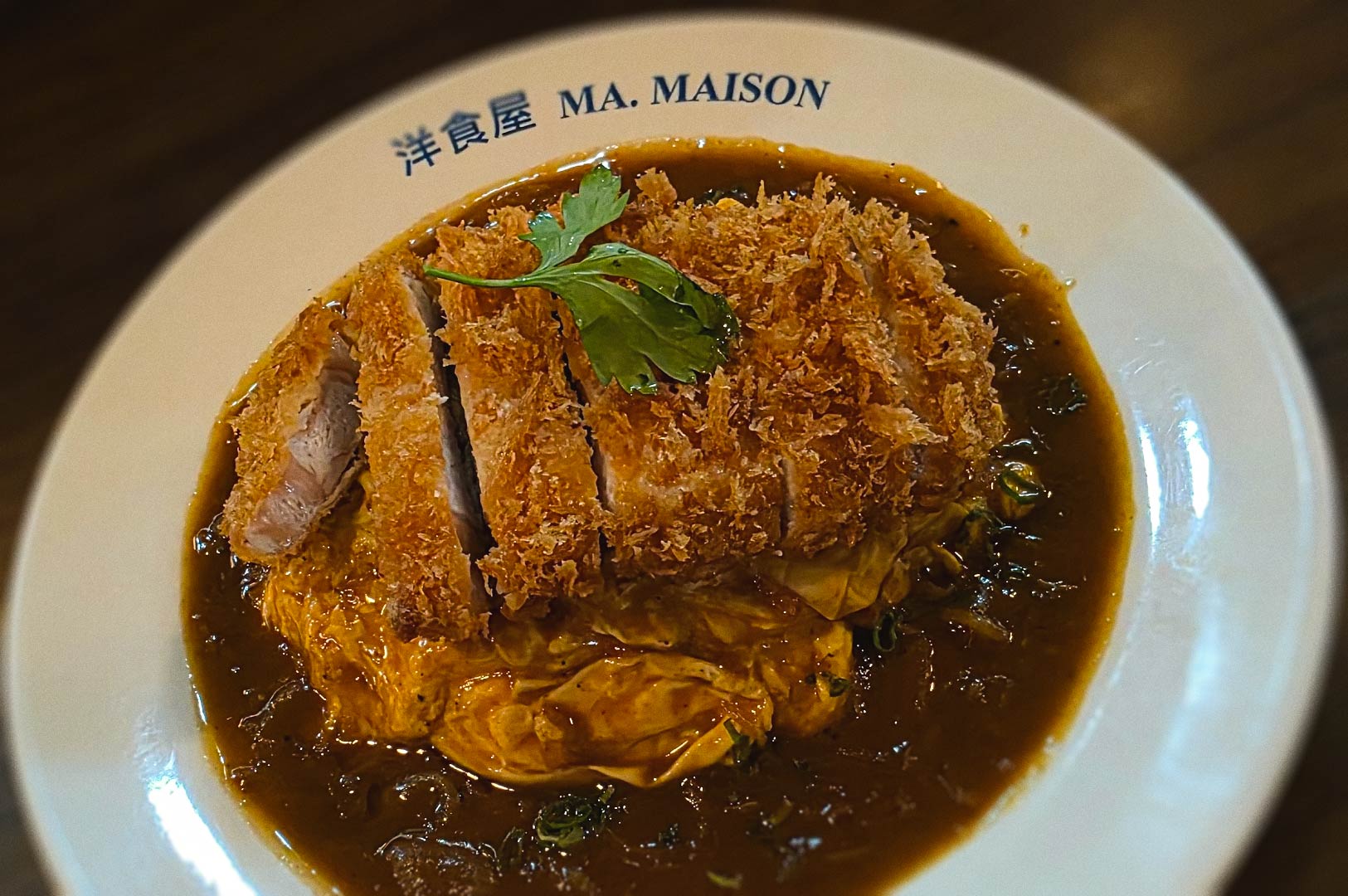 Crispy pork katsu served over fluffy omurice with savory Japanese curry sauce at Ma Maison.