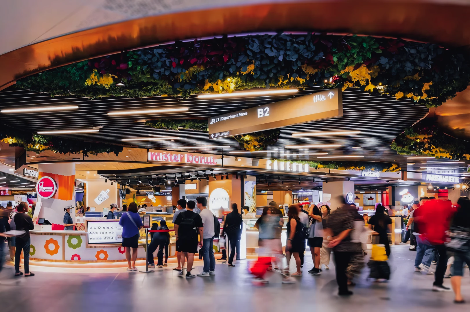 Wide‑angle interior shot of a vibrant shopping mall food court with multiple dining kiosks, illuminated signage, decorative ceiling greenery, and crowds moving through the space, capturing urban lifestyle dining and contemporary food hall design.