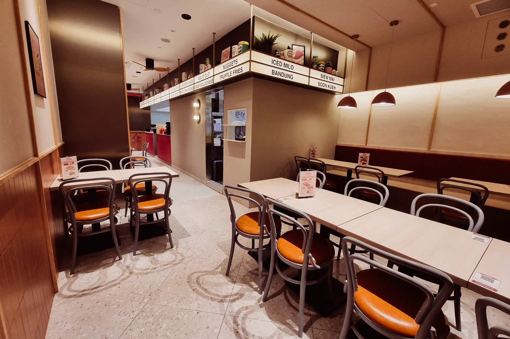 Wide-angle eye-level shot of Sally’s casual dining interior with neatly arranged tables, metal chairs with orange seats, warm lighting, and a compact modern layout inside a mall restaurant.