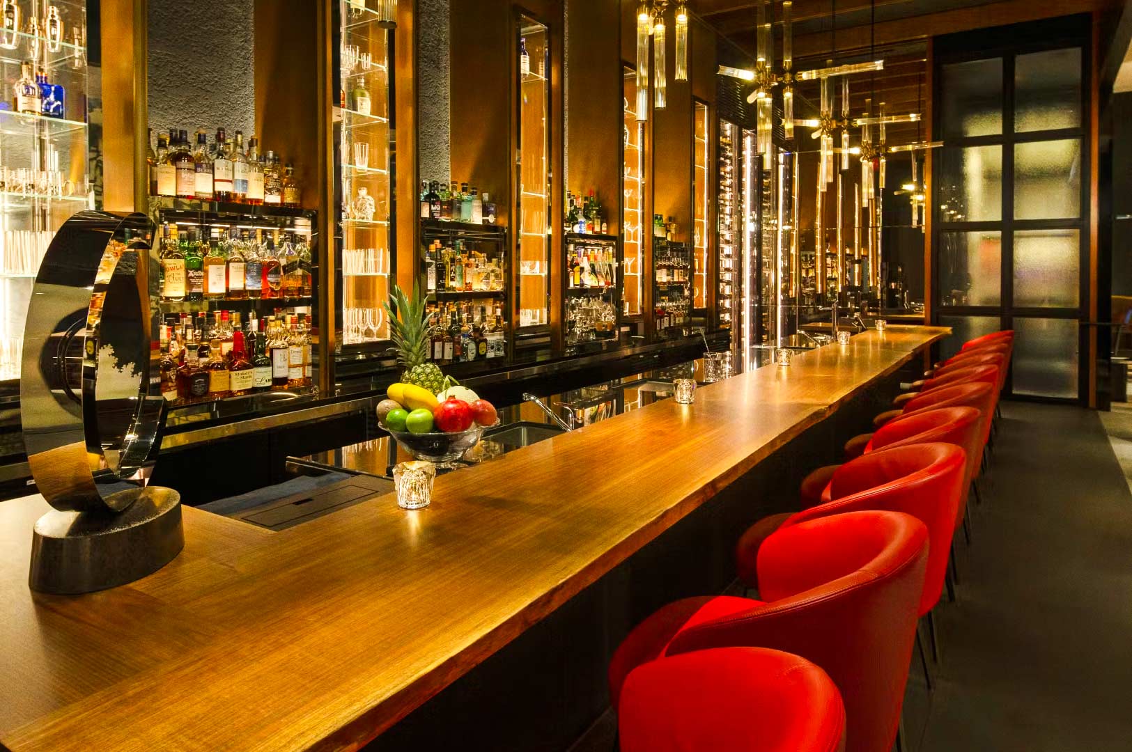 Luxury bar with long wooden counter and red seating.