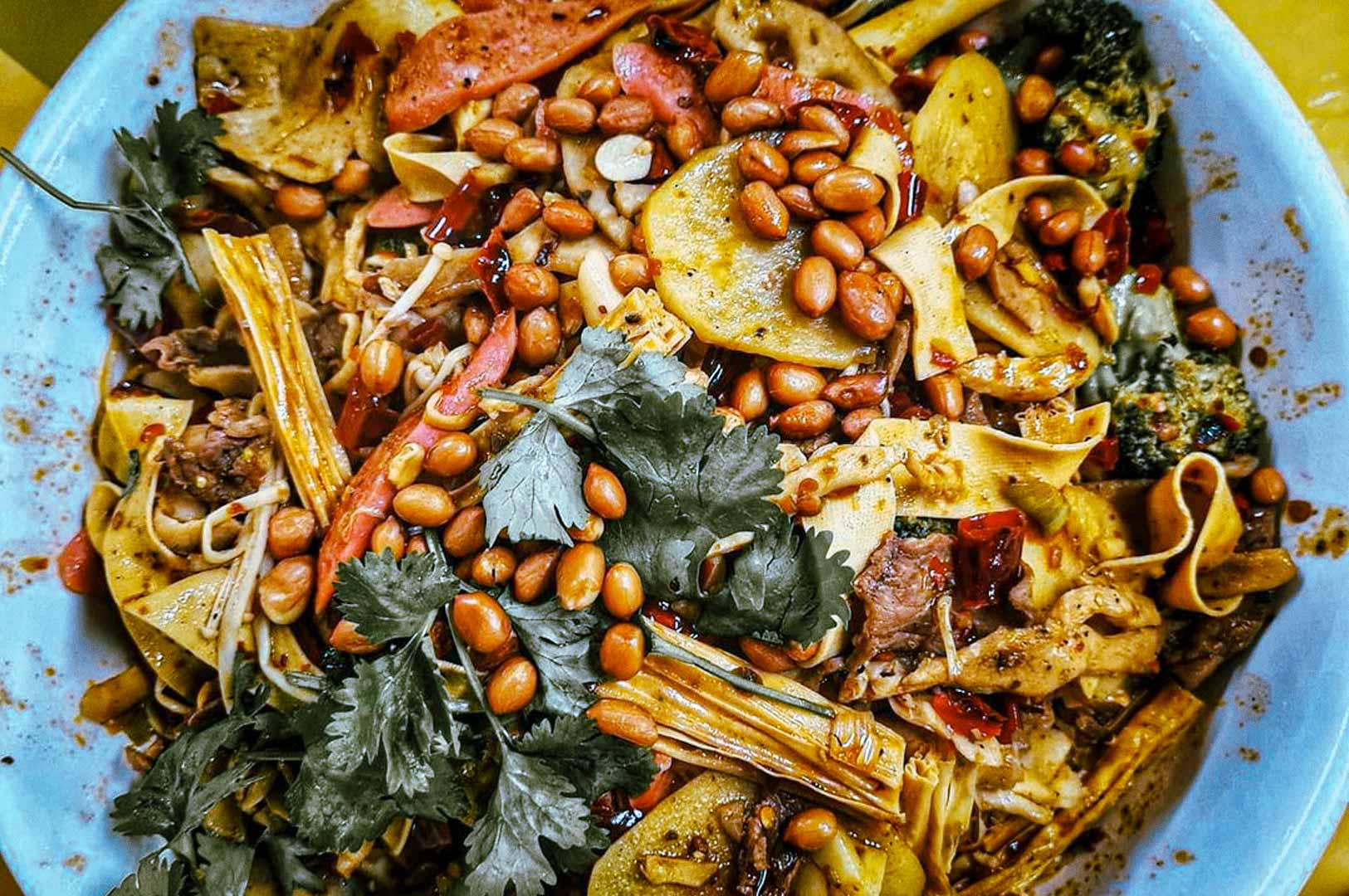 Plate of mala xiang guo with vegetables, noodles, and peanuts.