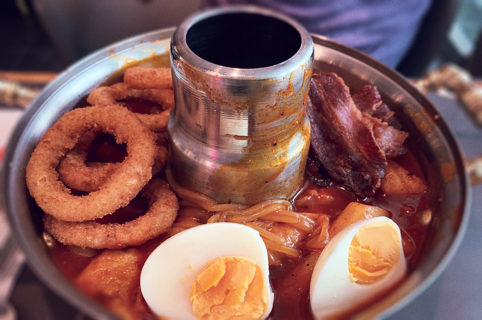Spicy Korean noodle soup (budae jjigae) in metal hot pot with halved eggs.