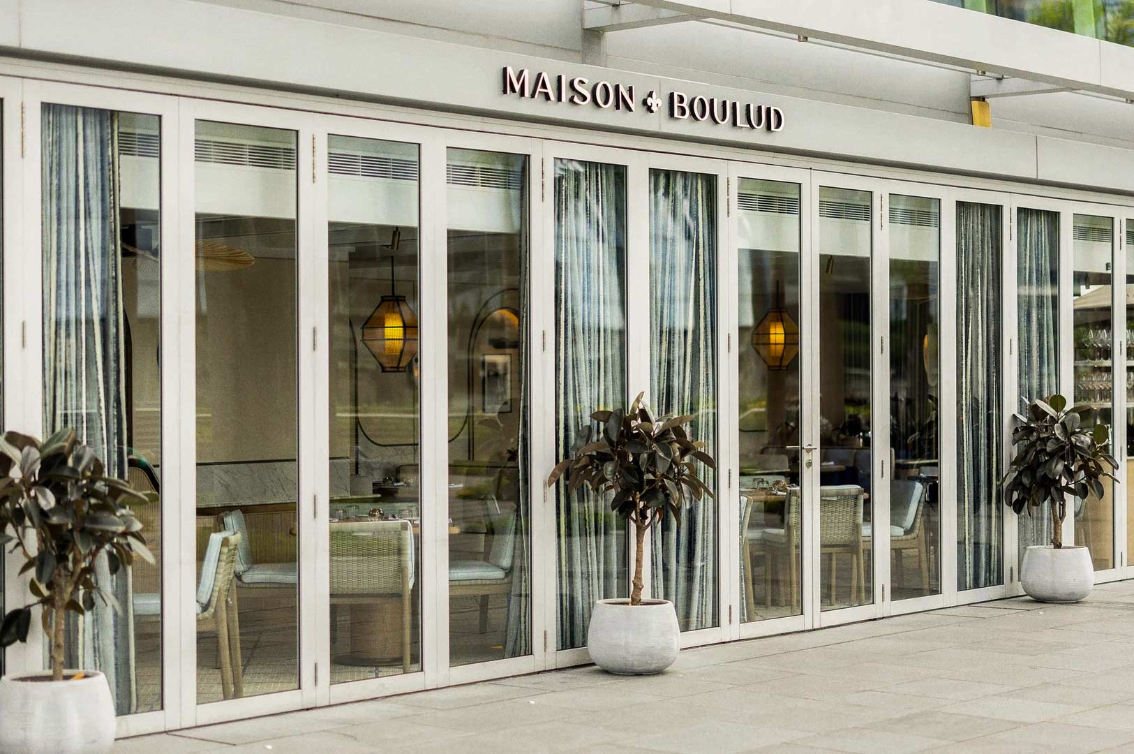 Bright restaurant facade with glass doors and potted plants.