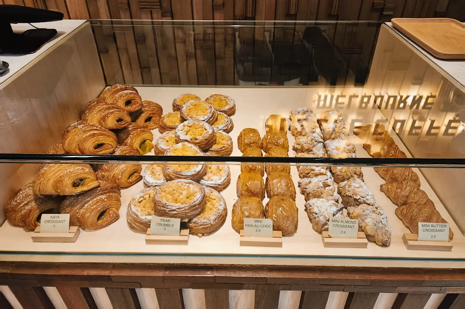 Straight-on medium shot of a glass pastry display at Puzzle Coffee showcasing croissants, tarts, and baked goods arranged neatly inside a modern café counter.