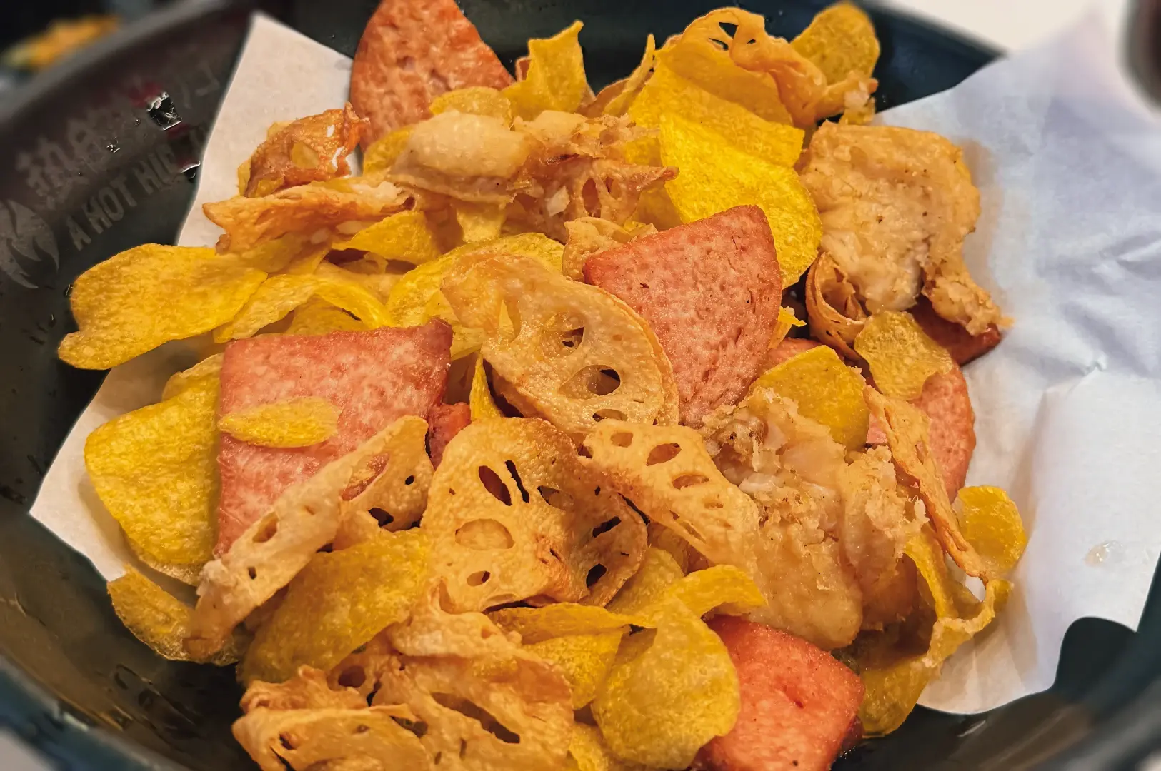 Close-up angled shot of deep fried mala sides at A Hot Hideout, including crispy lotus root chips, cheese tofu, and fried fish cake served as crunchy accompaniments to mala hotpot in Singapore.