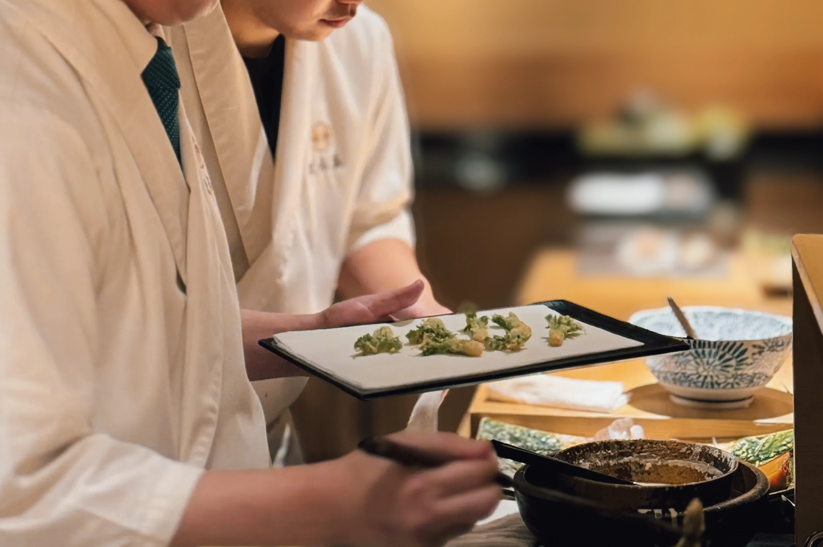 2 Tenshima Millenia Walk Medium close-up, side-angle shot of a Japanese chef plating seasonal tempura during an omakase service at Tenshima, Millenia Walk.