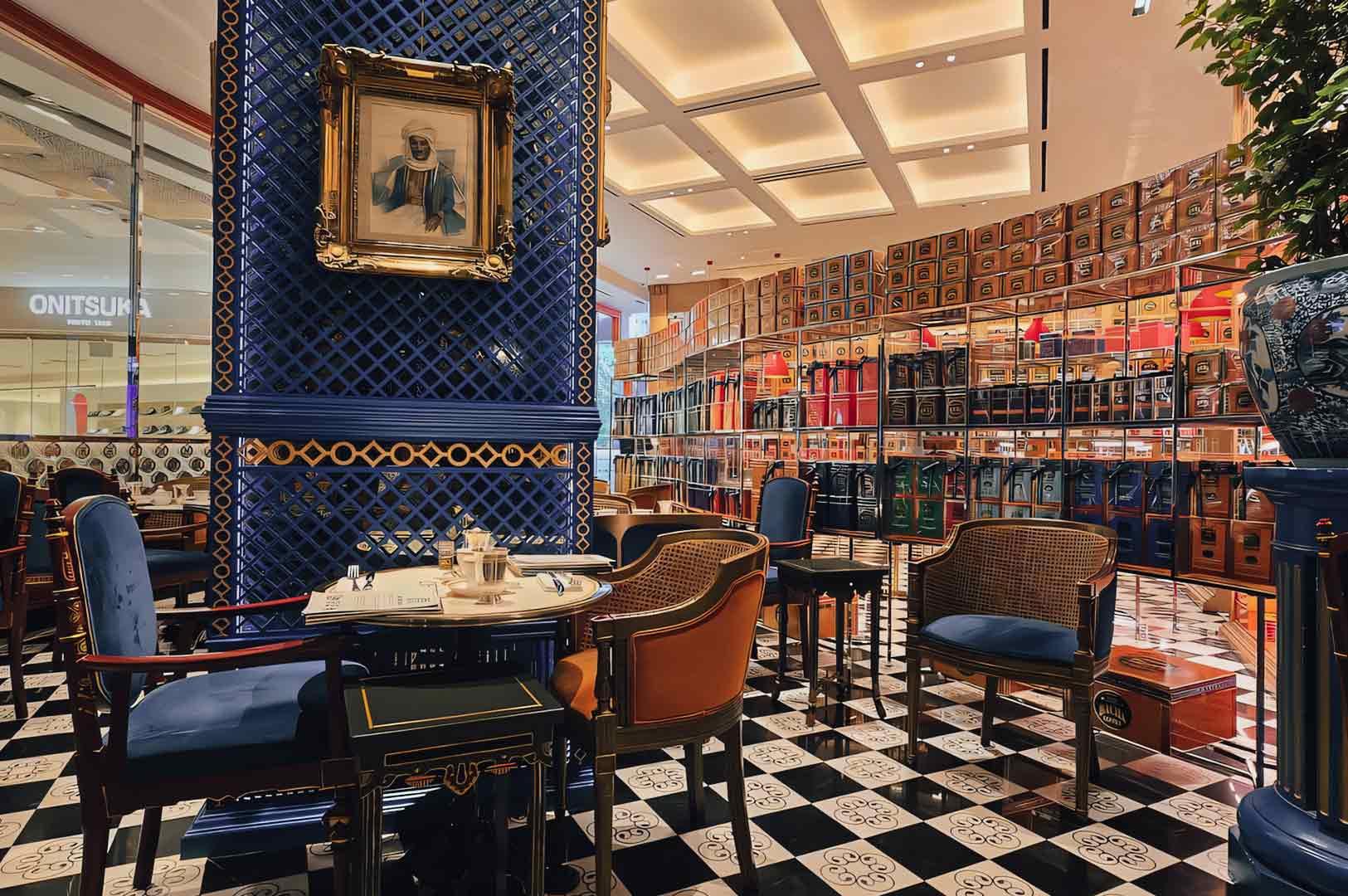 Wide interior shot of Bacha Coffee seating area with patterned tile floors, upholstered chairs, marble tables, and wall-to-wall coffee displays in an ornate café setting.