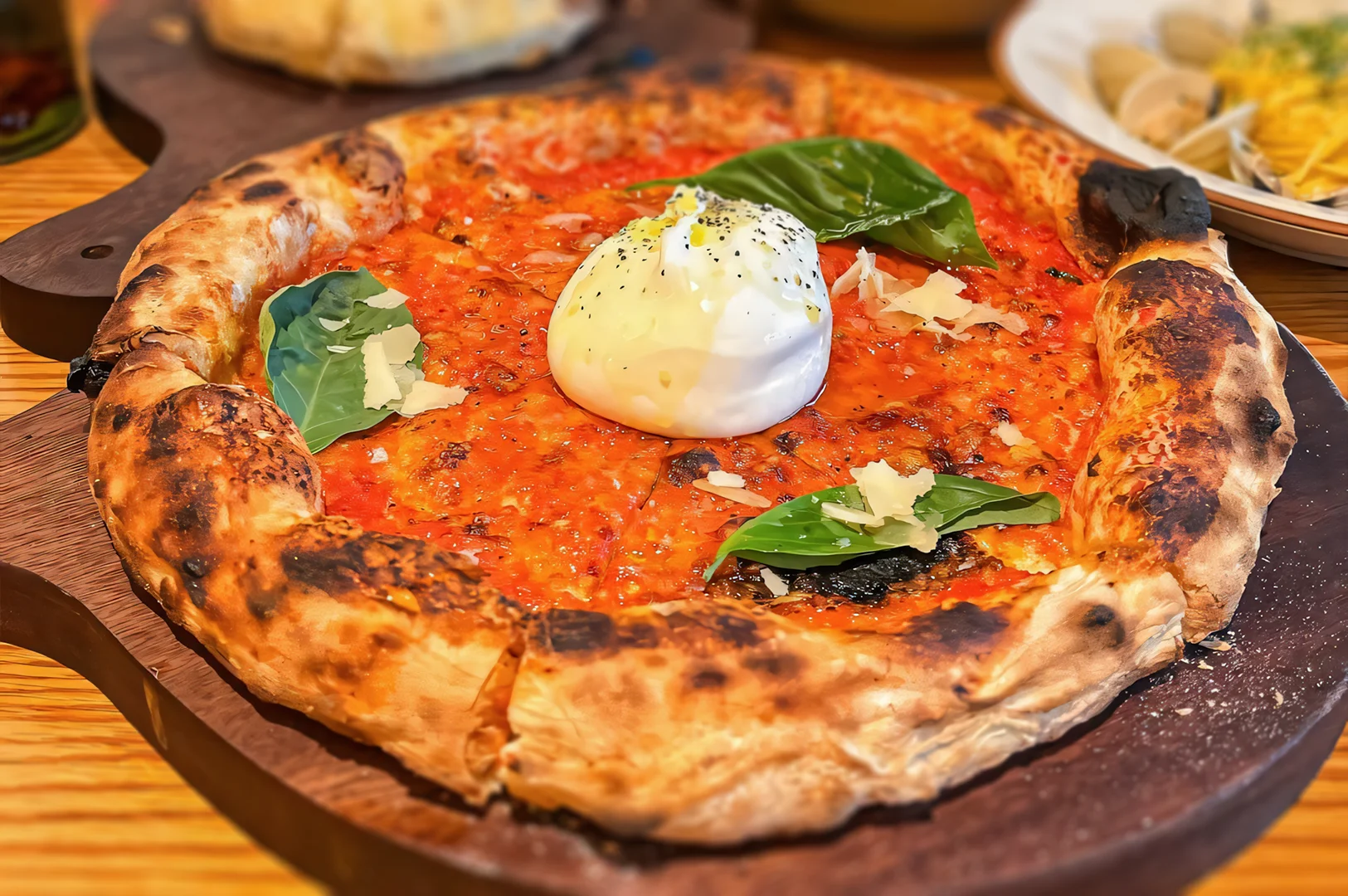 Close-up overhead shot of a freshly baked burrata pizza with charred crust, rich tomato sauce, creamy burrata cheese, fresh basil leaves, and grated parmesan served on a wooden board.