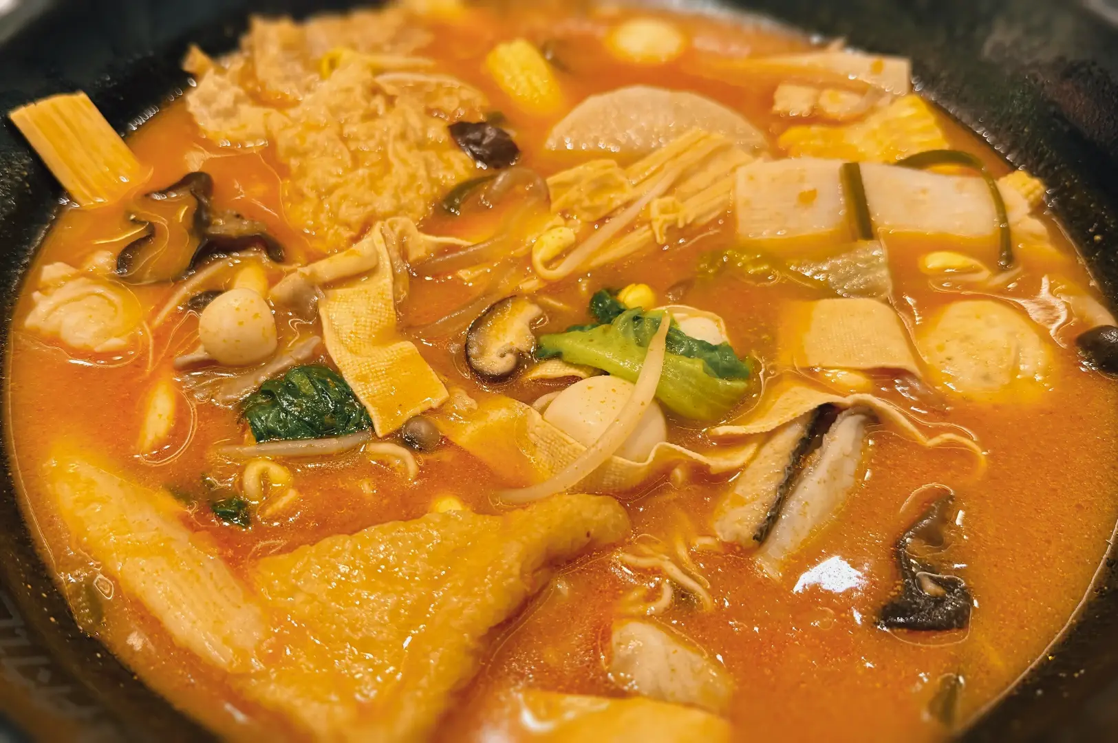 Top-down overhead shot of A Hot Hideout’s mala collagen soup, featuring chili-red broth with tofu skin, mushrooms, vegetables, and mixed mala ingredients in a steaming hotpot bowl.