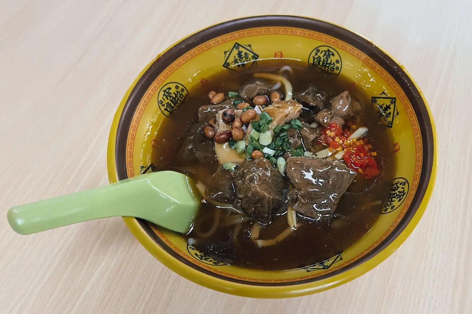 Top-down close-up shot of braised beef Hainan fen noodle soup with peanuts, chili, and herbs in rich dark gravy at People’s Park Complex food centre Chinatown Singapore