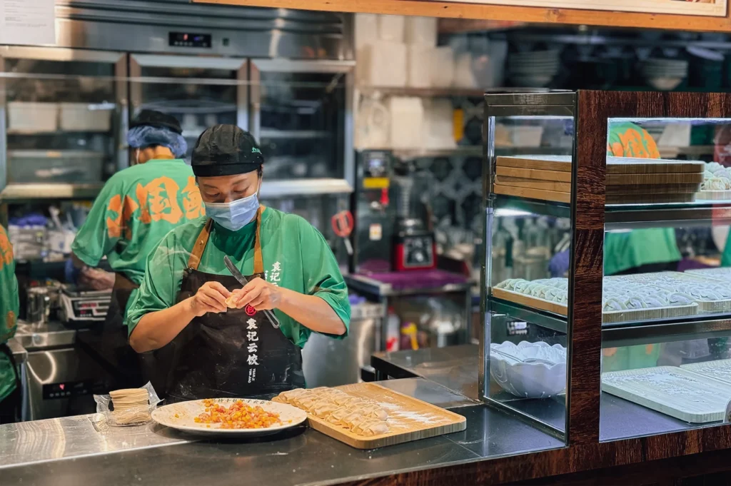 Medium eye-level shot of staff preparing handmade dumplings with fresh fillings beside tray of uncooked dumplings at Yuen Kee Fortune Centre.
