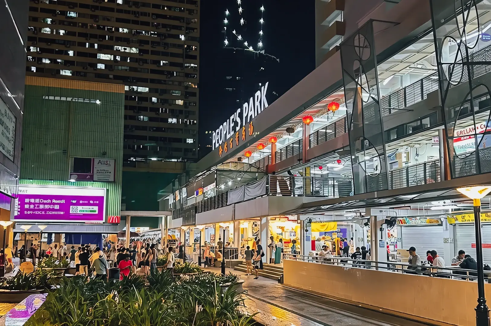 Wide-angle night street-level shot of People’s Park Complex Chinatown Singapore with illuminated signage, lantern-lit walkways, retail shops, and evening crowd activity