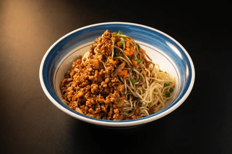 A close-up of a hearty, kid-friendly bowl of noodles generously topped with savory minced meat and fresh scallions, served in a traditional blue and white bowl.