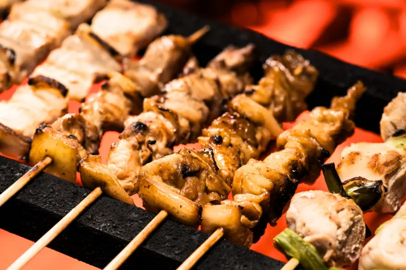 A close-up view of various chicken yakitori skewers sizzling on a hot grill over glowing red coals.