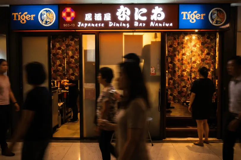 The glowing sign of Japanese Dining Bar Naniwa above the entrance, with patterned doorway curtains and the warm interior light contrasting against the blurred movement of passersby in the corridor.