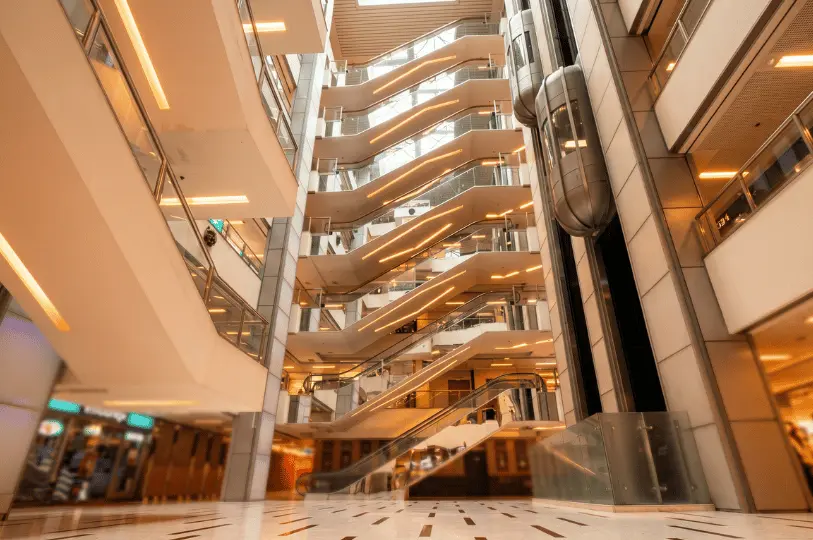 The multi-level interior atrium of Cuppage Plaza, showcasing a network of crisscrossing escalators and a glass elevator illuminated by warm architectural lighting.