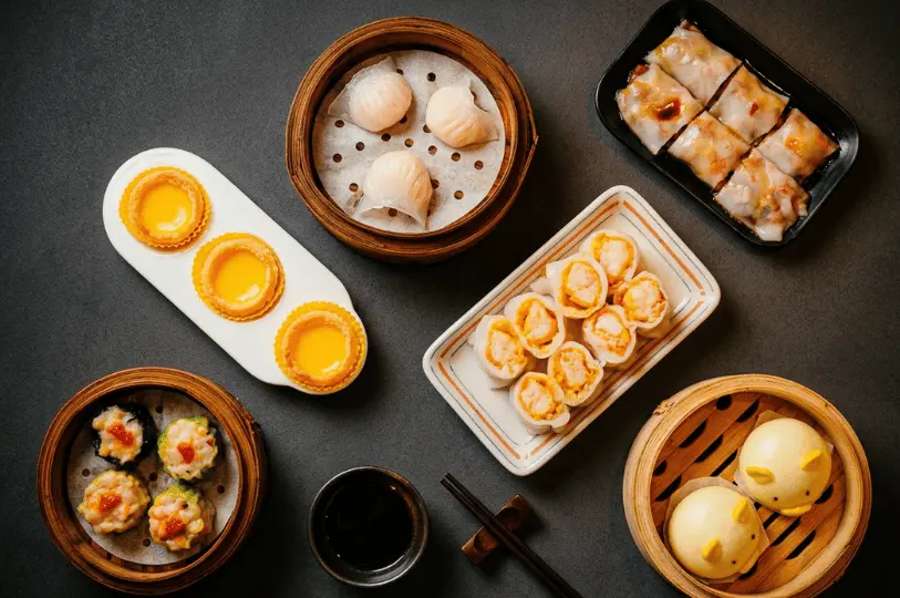 A top-down view of a varied dim sum feast perfect for sharing, featuring kid-friendly animal-shaped steamed buns alongside classic favorites like egg tarts, shrimp dumplings, siew mai, and rice noodle rolls.