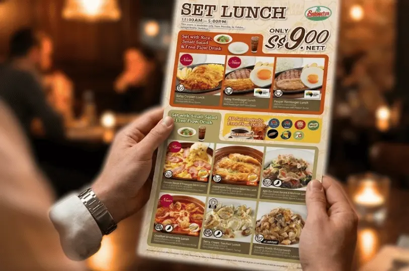 A close-up view of a customer holding the Saizeriya Set Lunch menu, showcasing various affordable meal combinations, including a main dish, side salad, and free-flow drink.