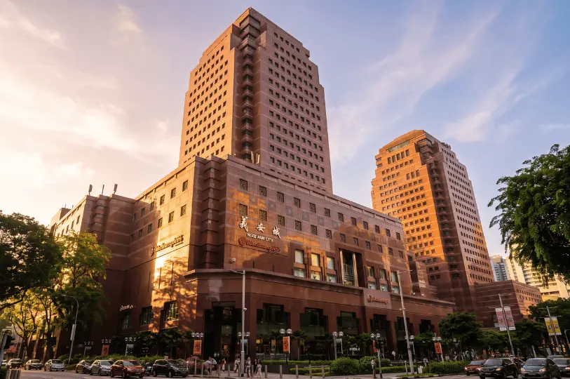 An exterior view of the iconic Ngee Ann City building on Orchard Road bathed in warm golden hour light, set against a soft sunset sky.