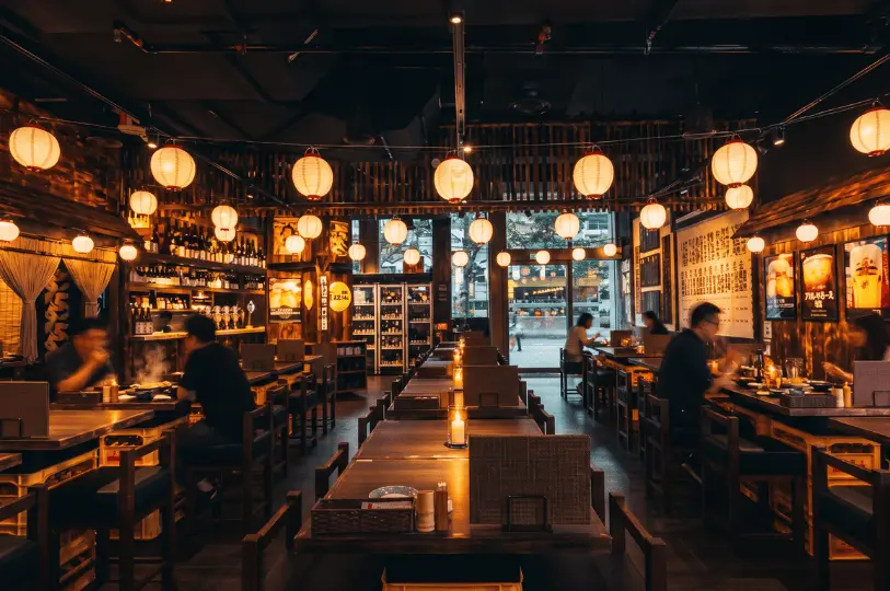 Bustling indoor dining room of The Public Izakaya by Hachi filled with patrons under rows of glowing Japanese paper lanterns.