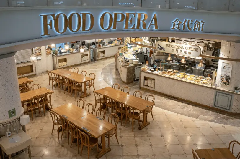 High-angle view of the Food Opera food court entrance at ION Orchard, featuring an illuminated sign above an Indonesian Padang stall and a quiet seating area with wooden furniture.