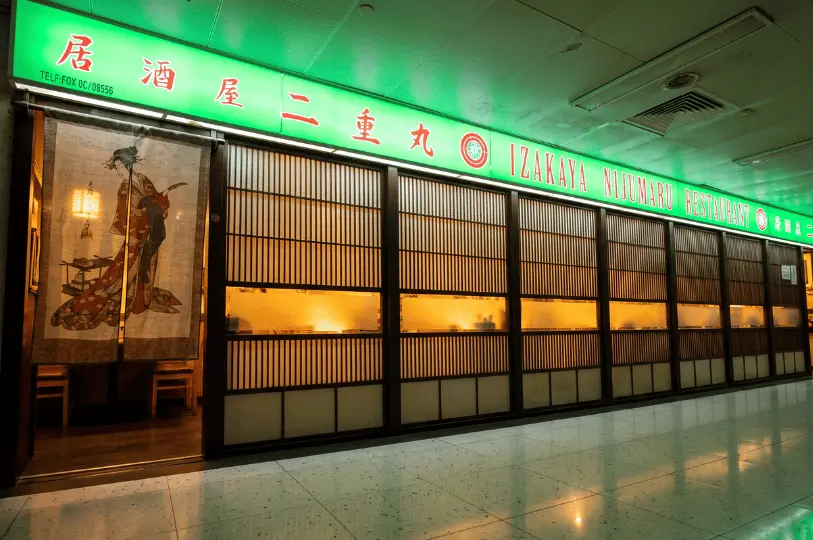 The traditional facade of Izakaya Nijumaru Restaurant at Cuppage Plaza, anchored by a bright green illuminated sign, wooden slatted sliding panels, and a doorway hung with a Japanese geisha tapestry curtain.