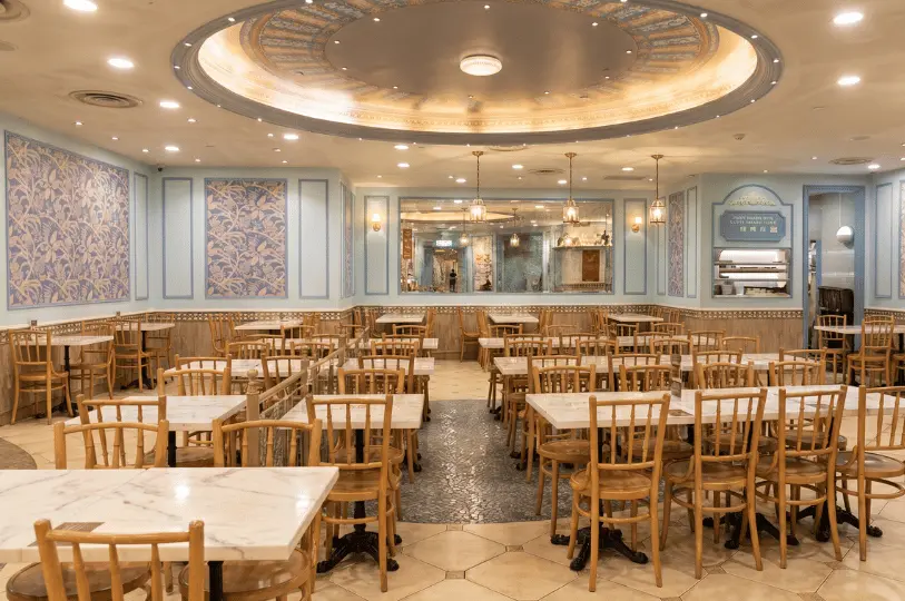 The elegant, nostalgic interior of the Food Opera dining area, highlighting pale blue walls with intricate floral panels, an ornate ceiling dome, and rows of empty marble-topped tables.