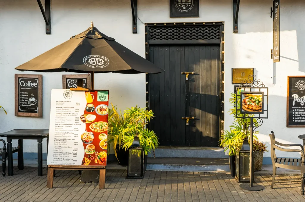 A restaurant exterior with white walls and black door, tables, and chairs with its menu displayed in front.