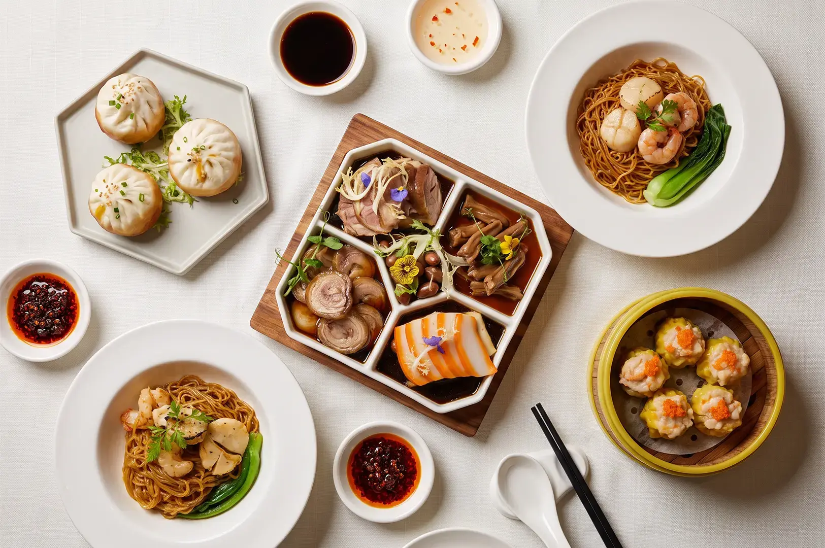 Flat lay wide show of Crystal Jade Golden Palace menu items including dim sum, noodles, set meal platter, and various sauces arranged on top of a white table.