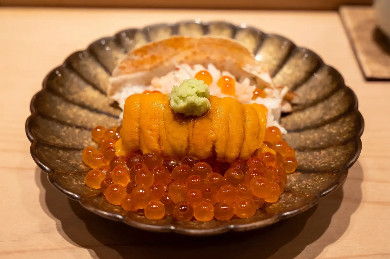 Ginza Sushi Ichi sushi prepped using sea urchin served on a round platter on a wooden countertop.