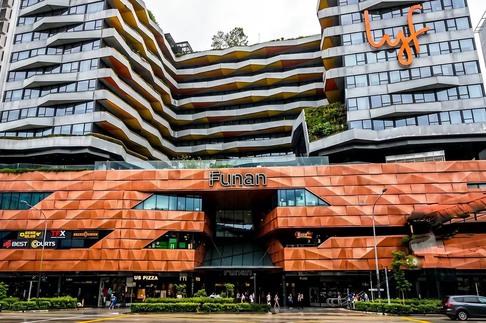 Wide angle shot of Funan Mall with orange and white tiles reflecting a bright sunny day and logo signage in the center.
