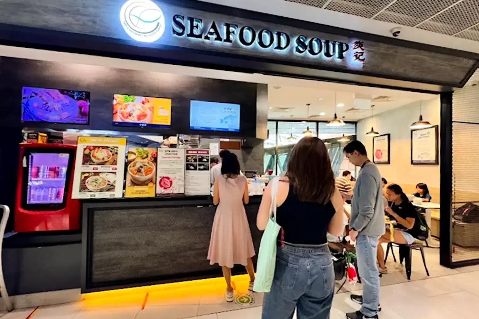 Yan Ji Gourmet Seafood Soup with customers lined up in front and dining inside, its counter filled with promotional displays and menu item screens.