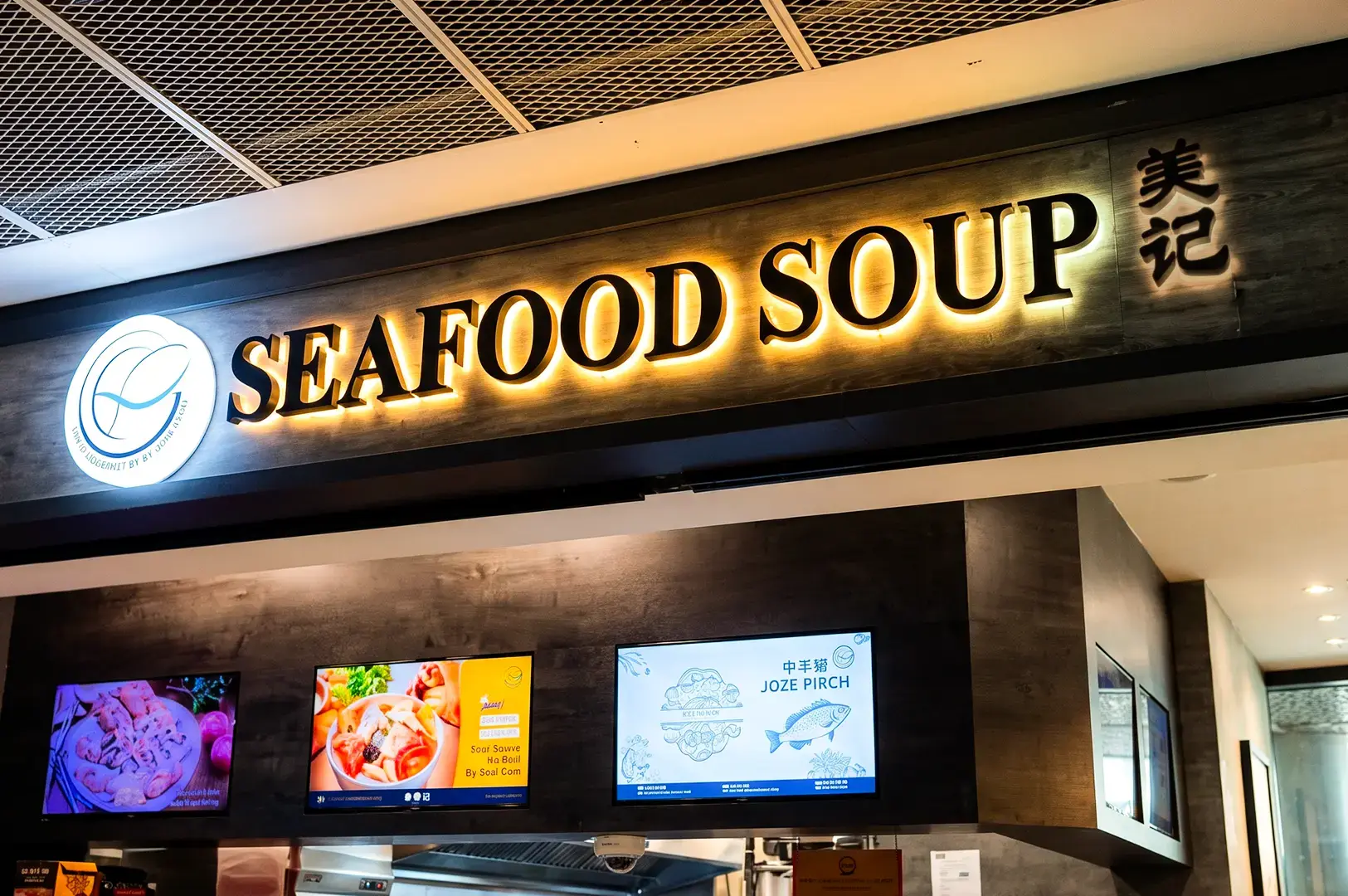 Zoomed in view of Yan Ji Gourmet Seafood Soup logo signage above their counter backlit with warm yellow and white lights.