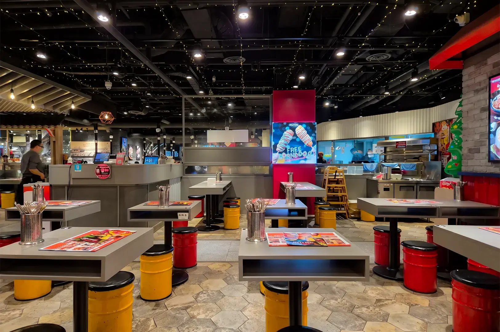Pocha Korean Street Dining interior with a empty square tables and round yellow and red chairs scattered around lined with bricked walls and white panels and a bare ceiling with white lights.