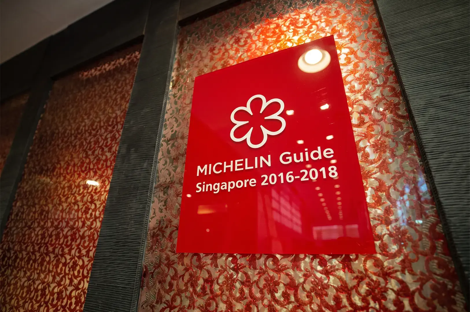 A red Michelin Guide plaque on a floral patterned wall with grey textured finishing.