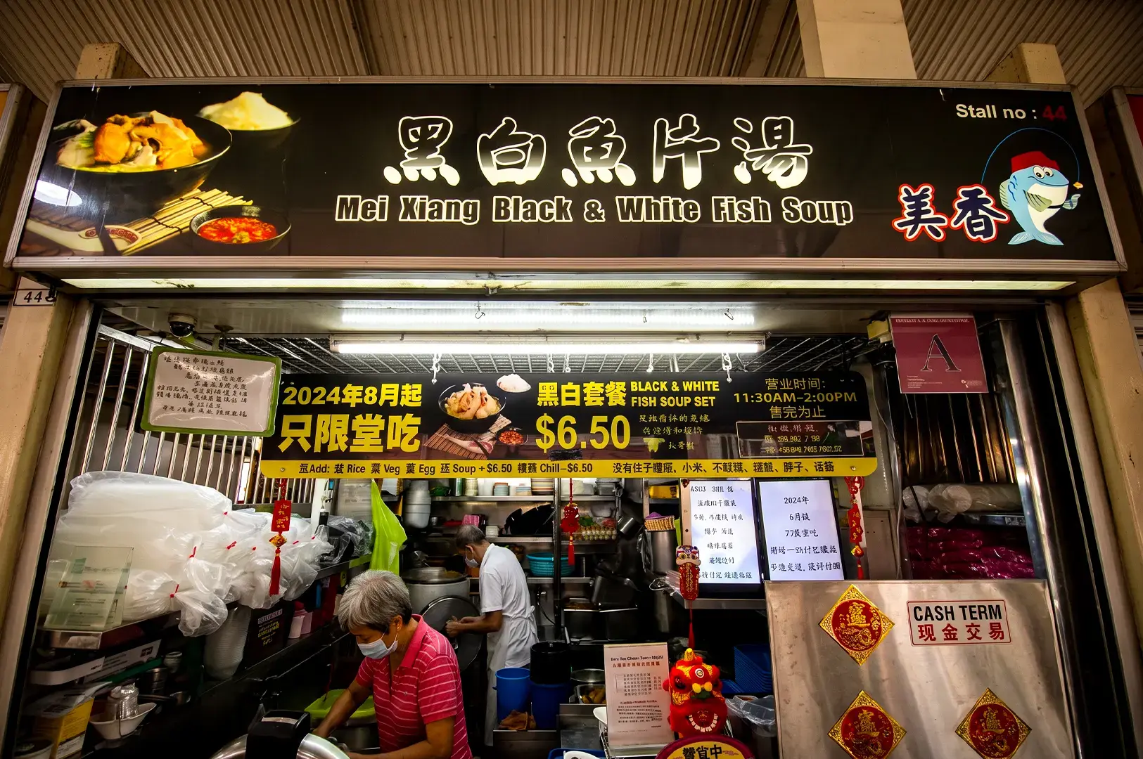 Mei Xiang Black & White Fish Soup store exterior. the long black rectangular signage showing their logo wand their menu signages visible at the store front with cooks preparing meals at the back.
