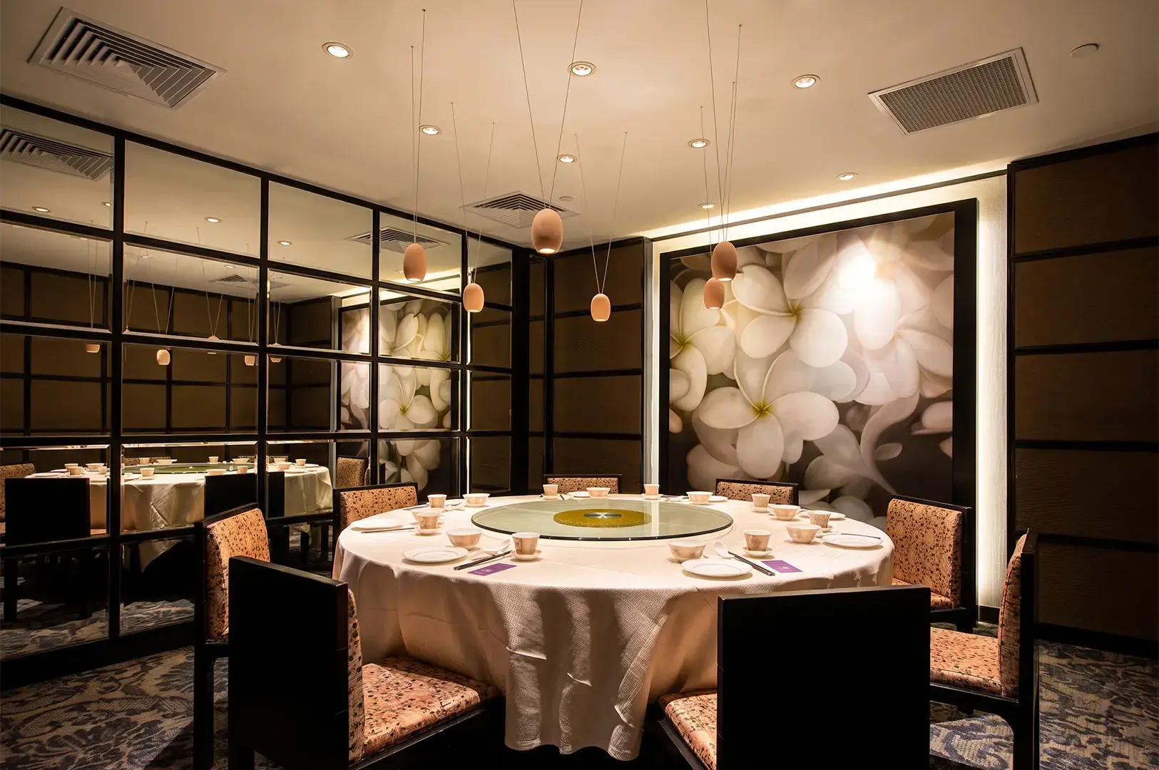 Crystal Jade Golden Palace interior with brown, white, and black colored chairs, tables, and walls, decorated with floral panels and illuminated with hanging warm lights.