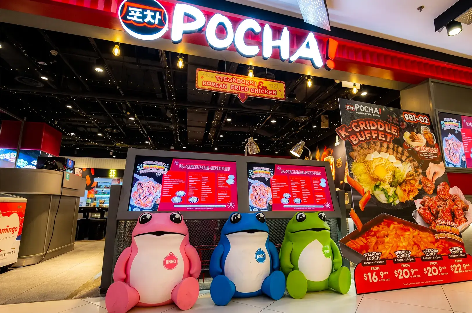 Pocha Korean Street Dining exterior with promotional posters and mascots lined up in front and the interior slightly visible behind lit by rows of white lights.